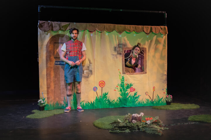 scenefoto van de kindervoorstelling Hans en Grietje. Met hans die voor het huisje van de heks staat.